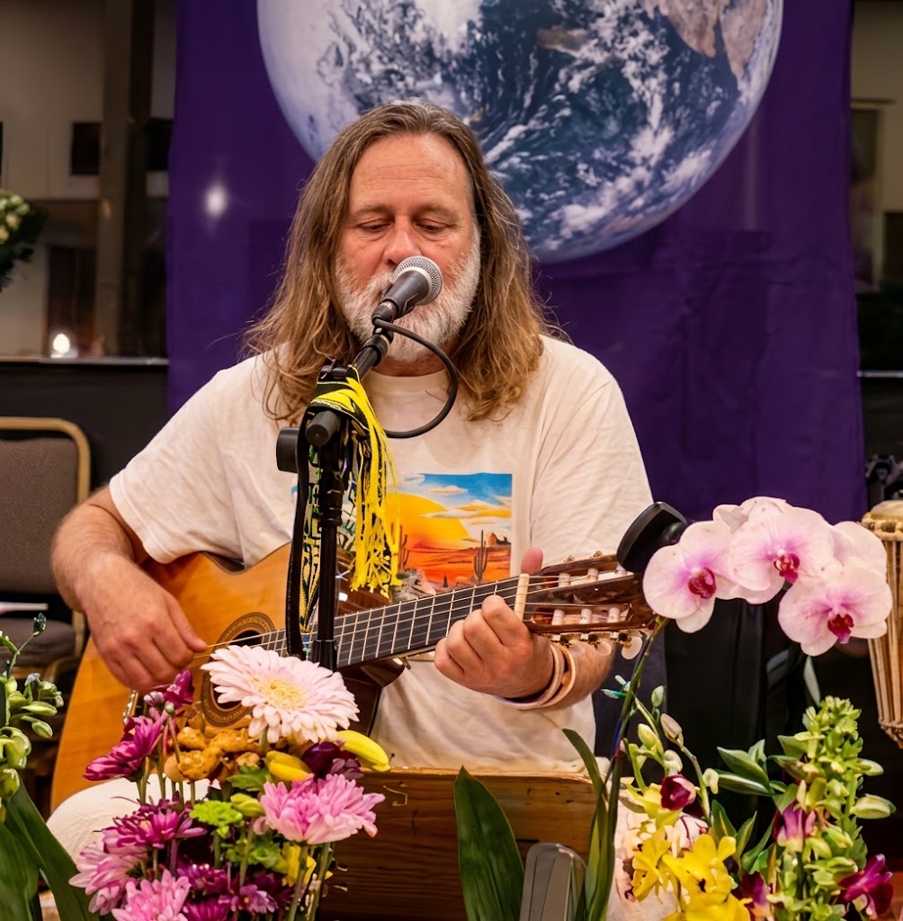 Lore Solaris singing and playing guitar at a microphone, flowers in the foreground and an image of the Earth behind him